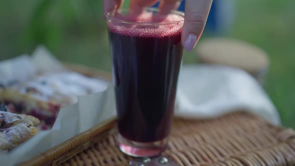Female Hand Putting Black Currant Juice in Glass on Picnic Basket in Slow Motion