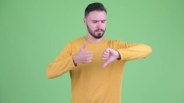 Confused Young Bearded Man Choosing Between Thumbs Up and Thumbs Down