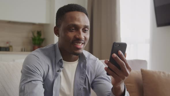 Happy African American Guy is Greeting His Friends on a Video Call and Waving His Hand in His