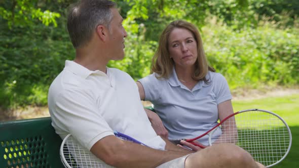 Mature couple outdoors take a break from playing tennis