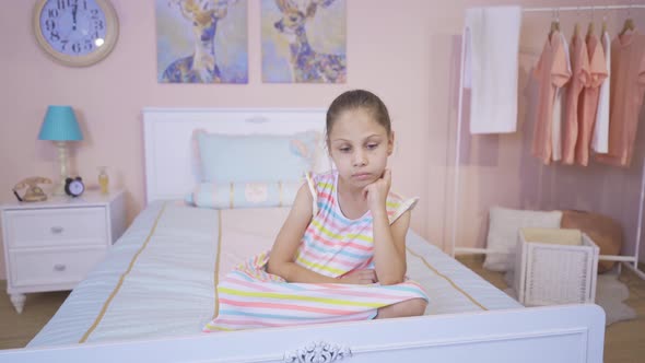 Thoughtful girl sitting on her bed. alt