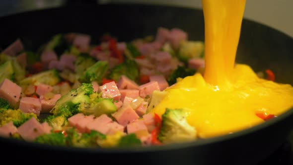 Pouring mixed eggs into a hot pan with vegetables, making a fresh and healthy omelet - Slowmotion