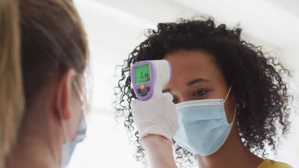 Woman wearing face mask getting her temperature measured at office