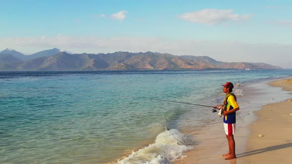 Fishing rod for good looking guy on a trip hanging out on beach on sunny blue and white sand 4K back