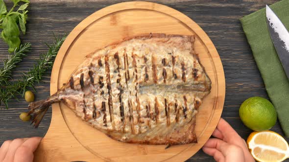 Hands are Placing a Wooden Board with a Delicious Grilled White Mackerel Fish