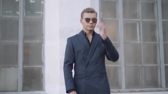 Portrait of Stylish Wealthy Young Man in Elegant Suit Putting on Sunglasses Outdoors