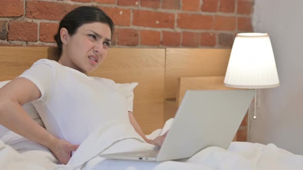 Young Indian Woman with Back Pain working on Laptop in Bed