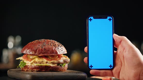Tasty Burger and Smartphone with Blue Chroma Key Screen Closeup Cooked Juicy Sandwich Fast Food