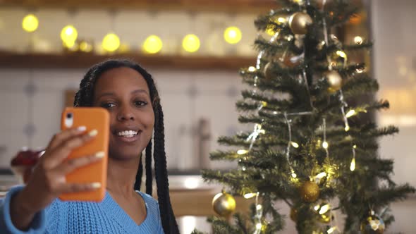 African Young Woman Showing Christmas Tree Decorations While Having a Video Call on Smartphone