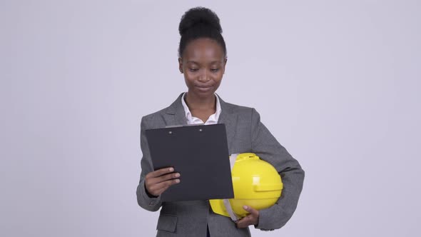 Young Happy African Businesswoman Holding Hardhat While Reading on Clipboard