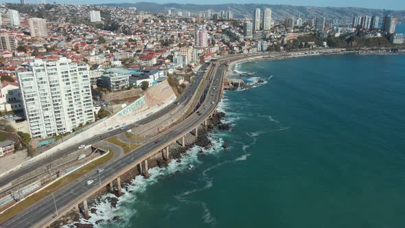 Aerial dolly in of traffic in avenue next to turquoise sea coastine, Viña del Mar city buildings and