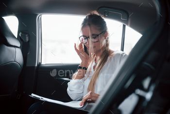 Turning pages. Smart businesswoman sits at backseat of the luxury car with black interior