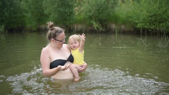 Little Funny Cute Blonde Girl Child Toddler in Yellow Bodysuit Laughing Learns Swim Outside at