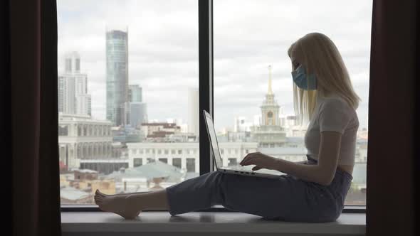 Young Woman Works Behind a Laptop in a Medical Mask