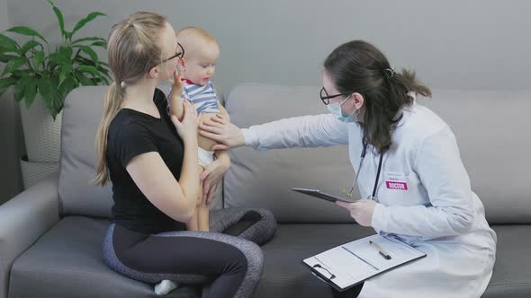 Female Doctor Woman Doing Check Up Examine Child Toddler with Mother Living Room