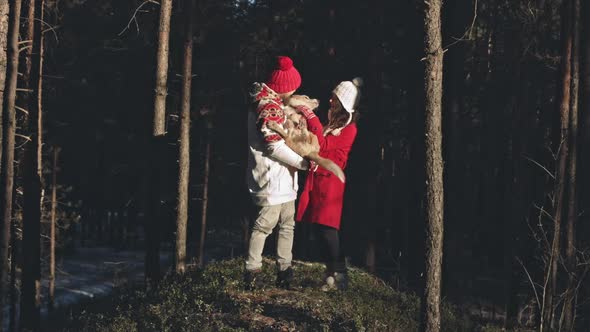 Happy Young Couple Hugging and Kissing in Winter Forest with Their Doggy