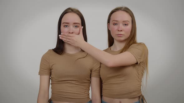 Front View Identical Twin Sisters Closing Mouth and Eyes of Each Other with Hand