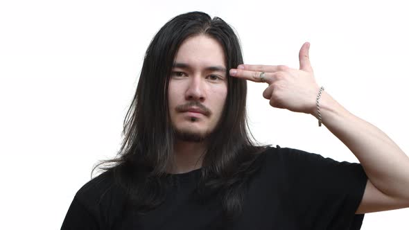 Closeup of Annoyed Eastasian Rocker Guy with Dark Long Hair and Piercing Pull Trigger on Finger Gun