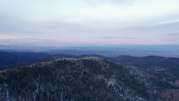 Drone shot high above a snowy-forest covered mountain during sunrise