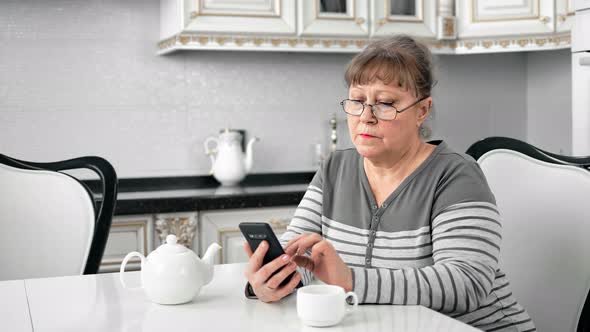 Mature Pretty Female in Glasses Thinking Using Smartphone at Cuisine Interior