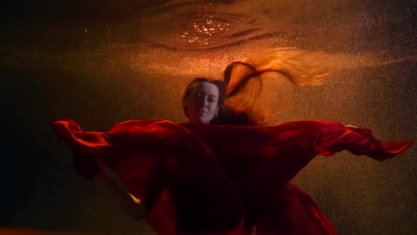 Portrait of a Girl in a Flowing Red Suit, She Is Underwater on an Orange Background with Bubbles and