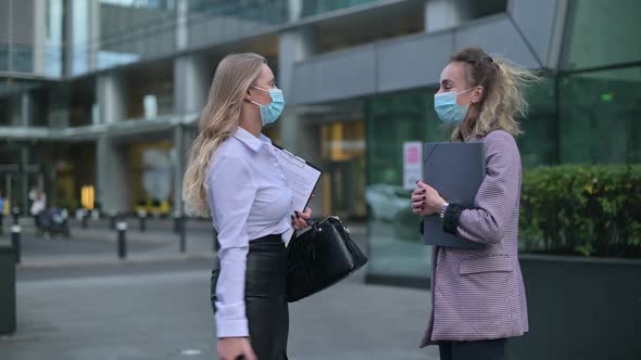 Two young business women wearing medical masks meet on the street to communicate