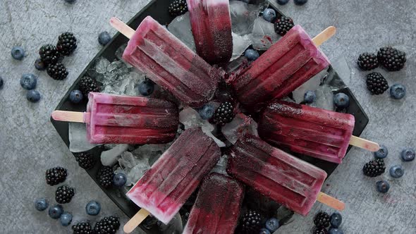 Homemade Fresh Frozen Blueberry and Blackberry Popsicles on Black Plate with Ice Sitting on Stone