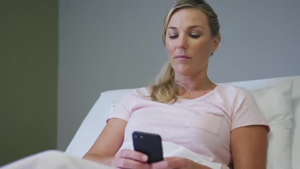 Caucasian female patient lying in hospital bed and using smartphone