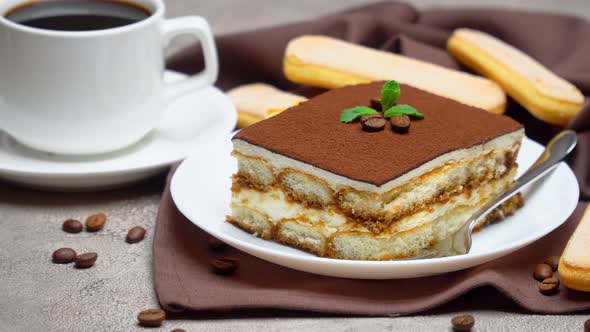 Portion of Traditional Italian Tiramisu dessert and cup of coffee on grey concrete background