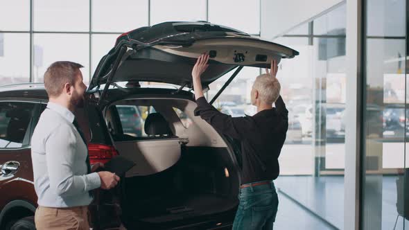 Adult Blond Caucasian Businesswoman with a Salesman Examines the Trunk of a New