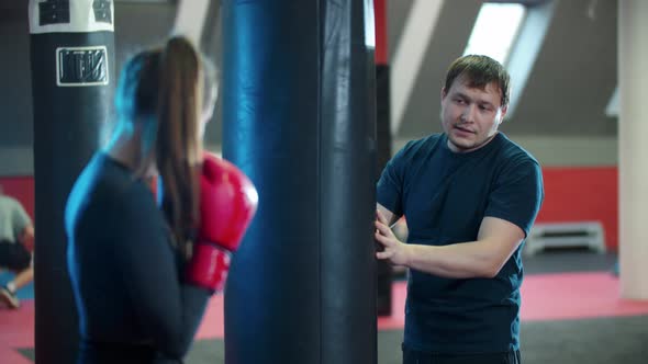 Boxing Training  Young Woman Punching the Bag and Her Coach Standing Behind It