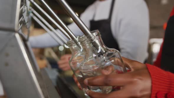 Midsection of two diverse colleagues at gin distillery filling and fastening lids on bottles by hand