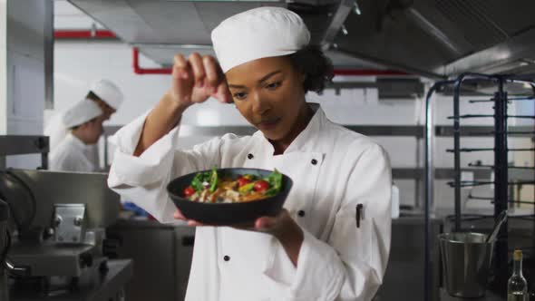 Portrait of african american female chef garnishing dish and looking at camera