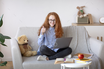 rl in eyeglasses showing thumbs up gesture sitting on the couch and using laptop, doing homework, recommending online school or educational course