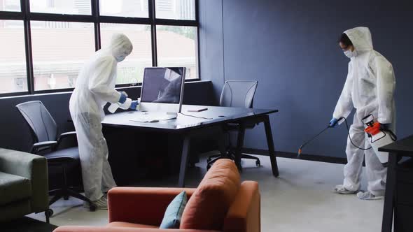 Cleaners wearing protective clothes sanitizing modern office space