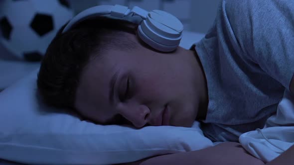 Male Teen in Headphones Sleeping at Home, Listening to Audio Book, Studying