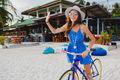 young attractive smiling woman in blue dress walking on tropical beach with bicycle - PhotoDune Item for Sale