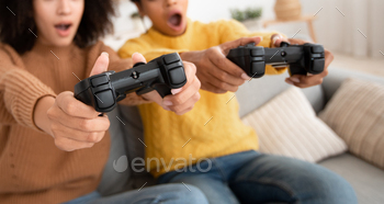 ile self-isolation. Surprised excited young african american women with open mouth with gamepads play in video game in living room, panorama, cropped