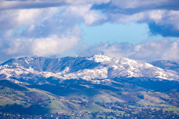 building on a sunny winter day; green hills in the foreground and snow covered peaks in the background; San Jose, south San Francisco bay, California