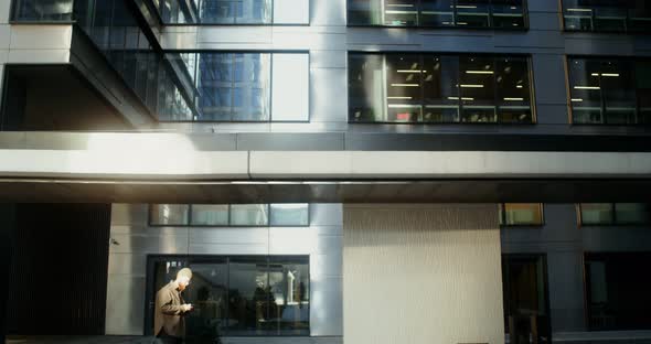 A Young Man is Typing on a Mobile Phone While Walking Around the Business Center