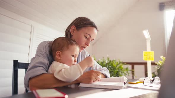 A Young Mother is Working at Home Using Computer While She's Taking Care of Her Baby