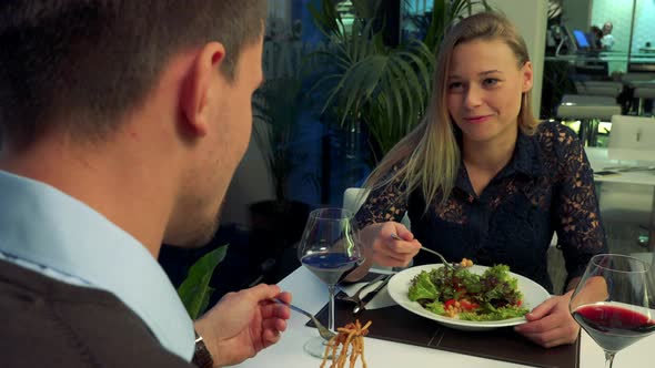 A Man and Woman Sit at a Table in a Restaurant, Eat and Talk