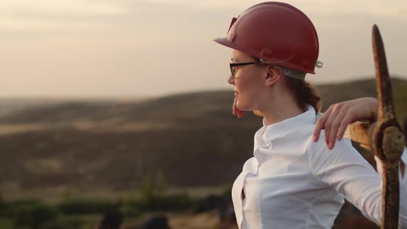 Businesswoman in Glasses Helmet and with Pickaxe on Her Shoulders Stands on Street Turns Herself