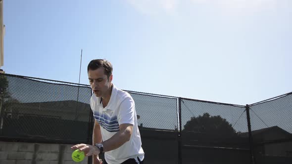 Wide angle low shot of a man serving a tennis ball.