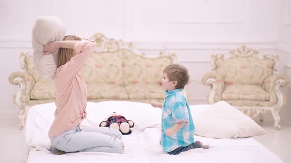 Mother and Son Jumping on the Bed and Throwing Pillows. Happy Family. Mother's Day. Child Support