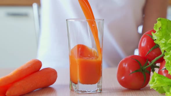 Woman Filling Glass of Fresh Carrot Juice in the Kitchen