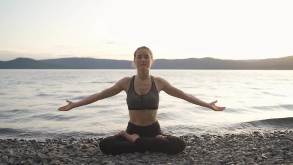 Young Attractive Girl Practices Yoga By the Lake at Sunset
