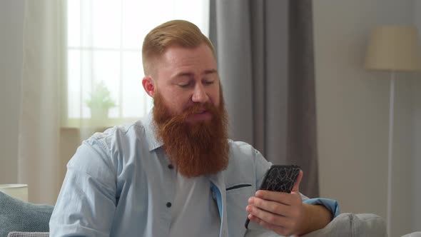 Happy Young Redhead Man Looking at Smartphone Screen Holding Web Camera Video Conversation with