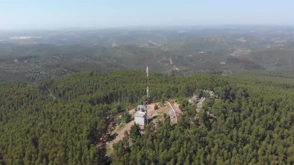 Descending aerial shot of Telecommunication Radio Tower Mast surrounded by natural forest trees