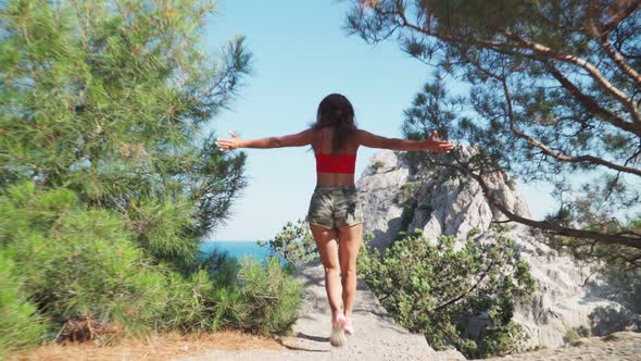 Beautiful Young Caucasian Girl Runs To Cliff Mountain Raises His Hands Up Against Sea